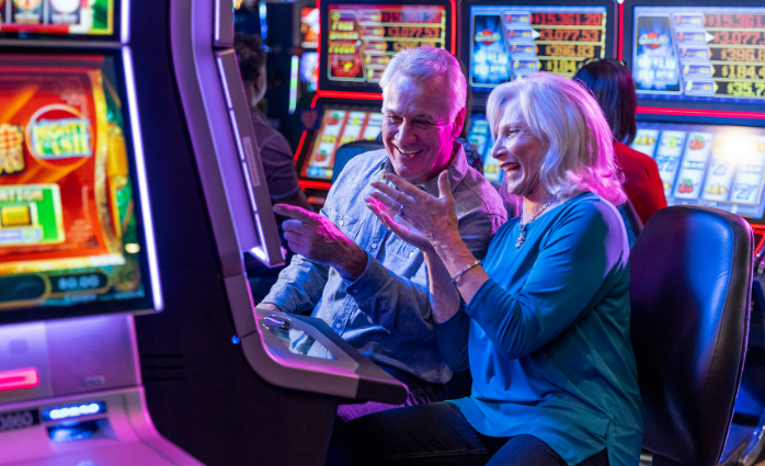 two old people a man and a woman sitting and looking happy while looking at a slot machine